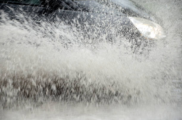 A car hidden in a large splash drives on a road that i flooded because of severe rainfall and bad kept drains.
