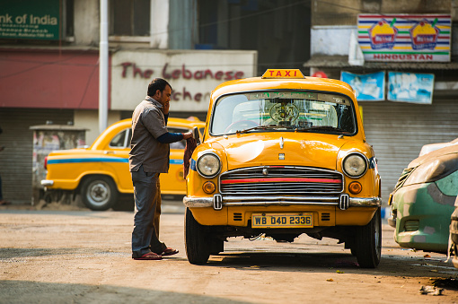 KOLKATA - INDIA - 21 Jan 2018: An Ambassador cab taxi drives he's washing his old yellow taxi at sunset. The Ambassador taxi is no more built by Hindustan Motors but thousands still remain on the streets of many India.