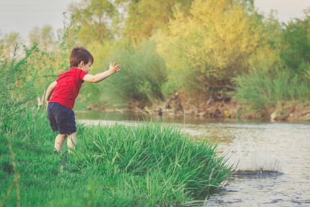 mały chłopiec rzuca kamieniem w rzekę - throwing stone little boys child zdjęcia i obrazy z banku zdjęć