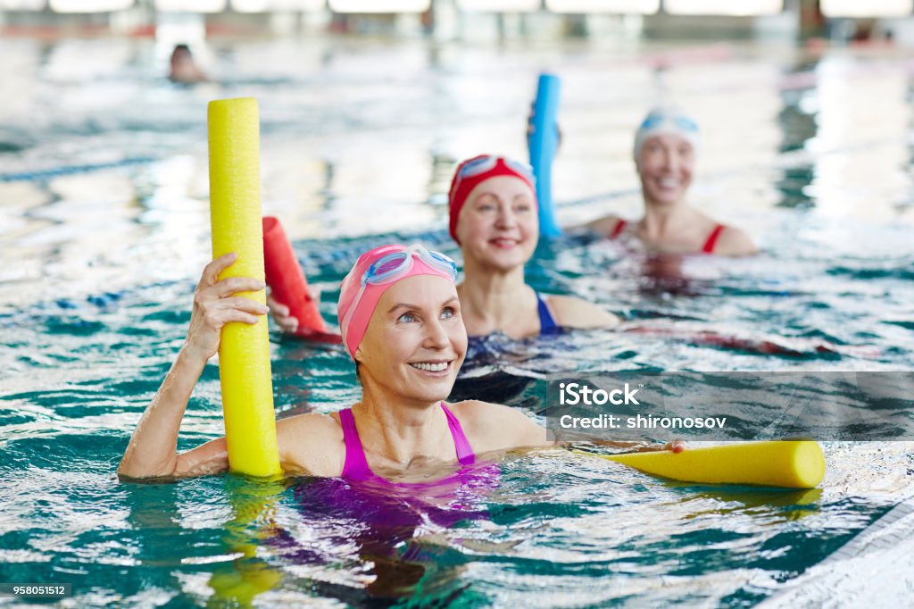 Aerobics in swimming pool Smiling mature female in swimwear and two more active women listening to trainer advice during gymnastics in water Exercising Stock Photo