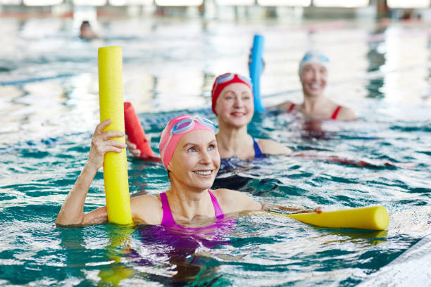 Aerobics in swimming pool Smiling mature female in swimwear and two more active women listening to trainer advice during gymnastics in water aerobics photos stock pictures, royalty-free photos & images