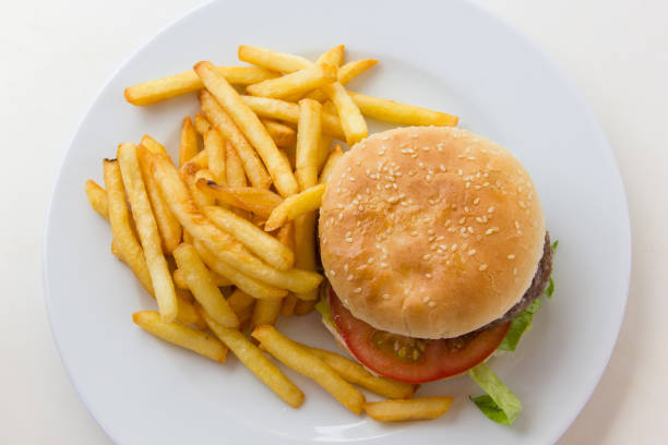 Top view of tasty beef burger with french fries on the side Hamburger with tomato, lettuce and potatoes on white plate from above. Poor nutritional meal concept dangerous steak stock pictures, royalty-free photos & images