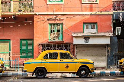 KOLKATA - INDIA - 22 Jan 2018: An Ambassador yellow cab taxi is parked in the street under a red-colored house in Kolcata, India