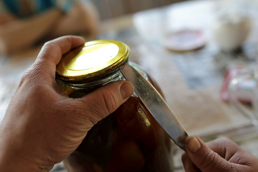 Person opening jar with pickled tomatoes at home
