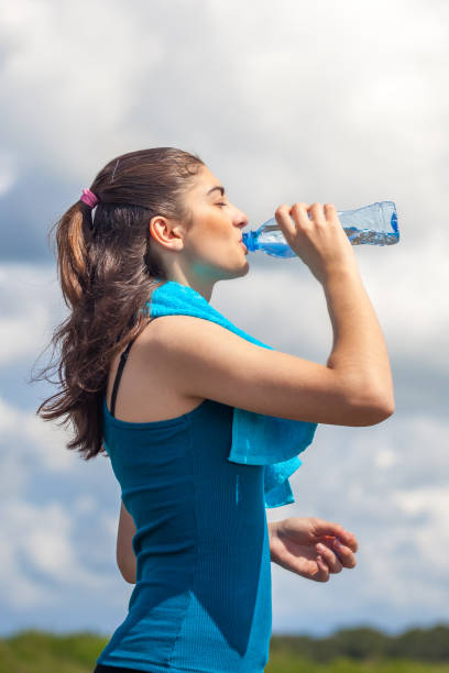 istock Beautifull girl runner is having break, drinking water against clear blue sky background 958071444