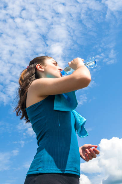 istock Beautifull girl runner is having break, drinking water against clear blue sky background 958073546