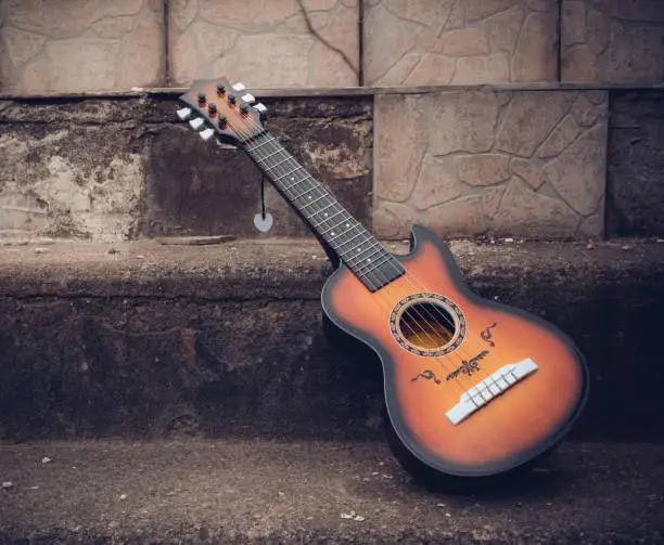 Wooden acoustic guitar outdoors in a street propped against the side of an old stone building on the sidewalk