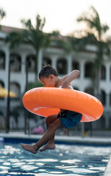 istock Excited little boy on vacation jumping into the pool with his inflatable ring 958126542