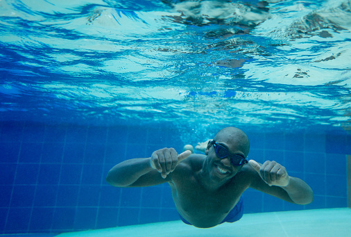 Portrait of black young man having fun at the pool under water smiling at camera very happy with thumbs up