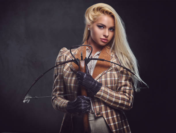 istock Studio portrait of blond old fashioned female holds a crossbow. 958132016