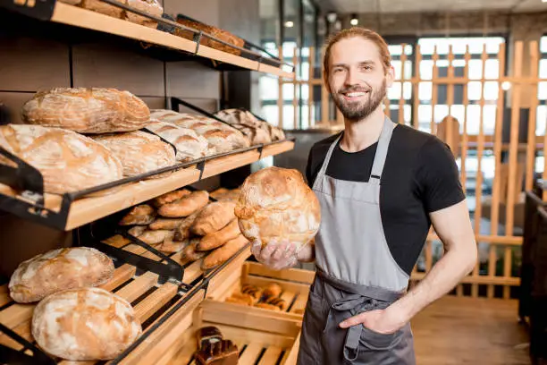 Portrait of a handsome seller in uniform standing with bread at the bakery shop