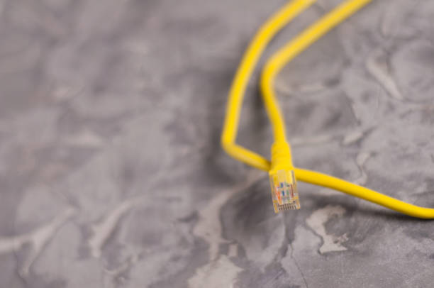 istock Yellow network cable for computer with plastic connector on old worn and scratched concrete floor with copy space 958143586
