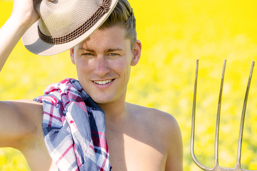 portrait of handsome man with pitchfork standing in front of yellow field