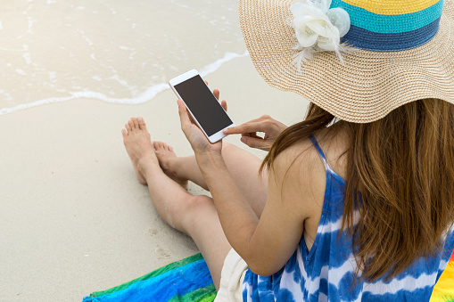 Young woman relaxing and using mobile phone at the tropical beach, Summer vacation and travel concept