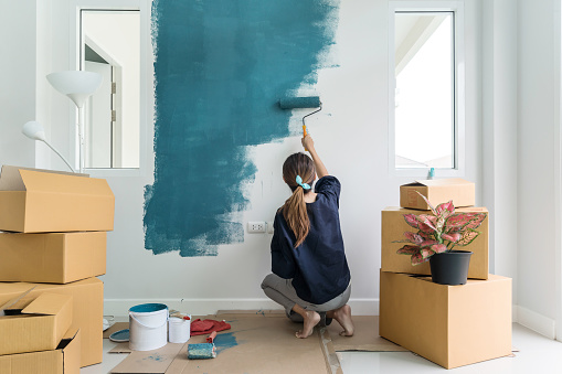 Young asian happy woman painting interior wall with paint roller in new house