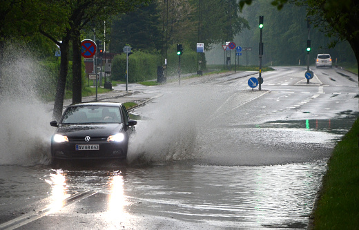 Sonderborg, Denmark - May 10, 2018:  A car splashes trough water on a road that is flooded afther a heavy rainfall. .