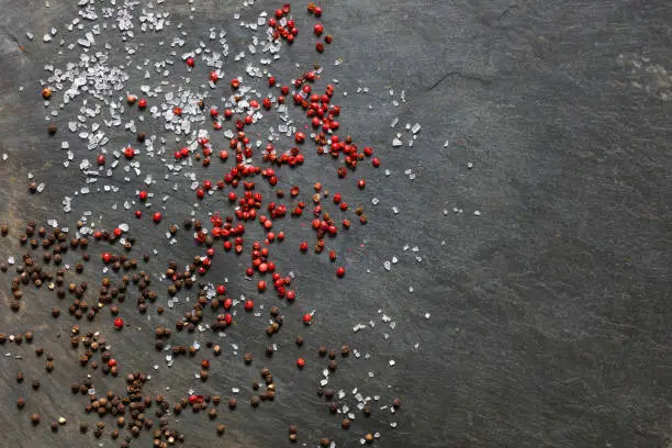 Rock sea salt  scattered with brown and pink peppercorns on slate background with copy space to right