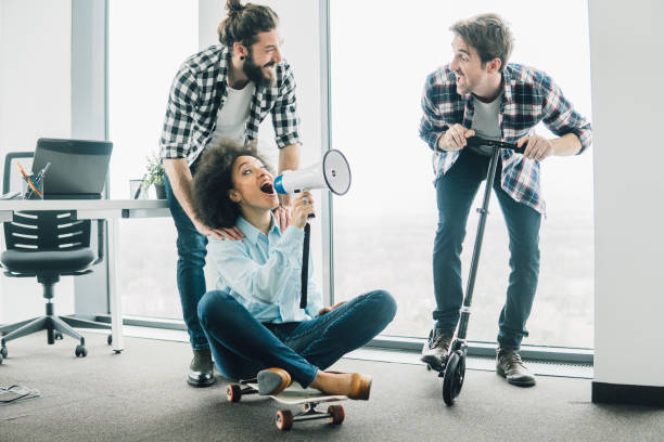 istock Coworkers having fun with megaphone, scooter and skateboard at office 958174474