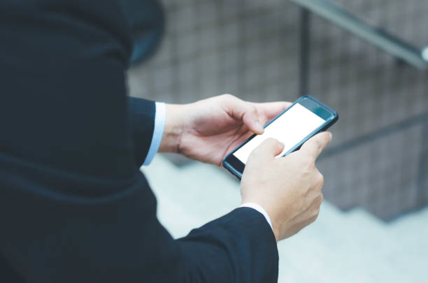 istock attractive business man holding smartphone white screen in hand touching using searching online technology wireless social media connecting world wide web at outdoor front of office building. 958188546