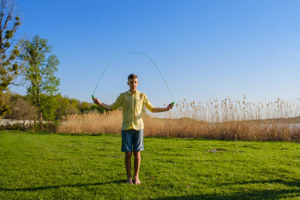 istock Young caucasian boy is doing workout with jumping rope on green grass lawn 958196276