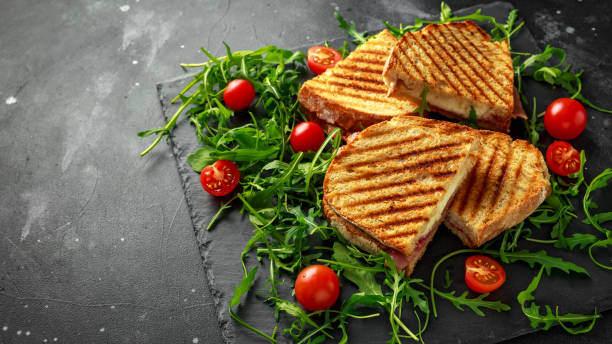istock Grilled Bacon, cheese sandwich and served on stone platter with arugula and tomatoes 958213034