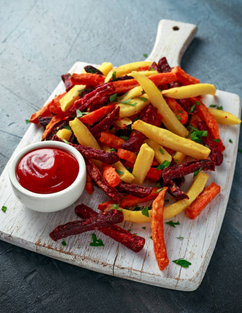 Homemade Baked Mixed Vegetable Fries beetroot, carrot and parsnip with ketchup. on white wooden board