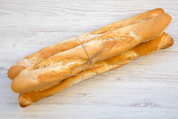 istock Fresh Baguettes on white wooden background, top view. 958224936