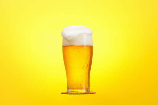 Glass of beer close-up with froth over yellow, background