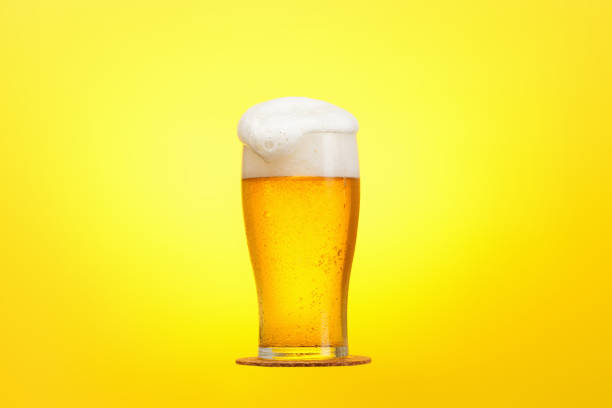 Glass of beer close-up with froth over yellow background stock photo