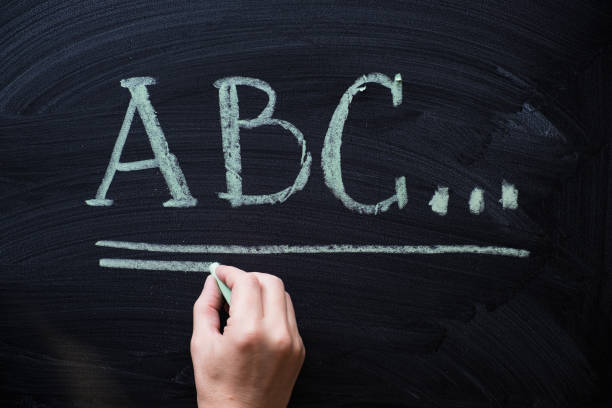 istock Female hand writing alphabet on black chalkboard. Educational background with ABC letters with copy space 958237526