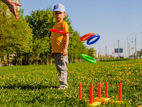 Little child boy playing. Ring throw summer game on a green lawn in the sun made of plastic