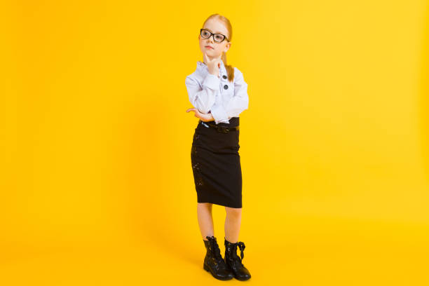 Girl with red hair on a yellow background. A charming girl in transparent glasses put a finger to her chin. Portrait of a beautiful girl in a white blouse and black skirt. see through leggings stock pictures, royalty-free photos & images