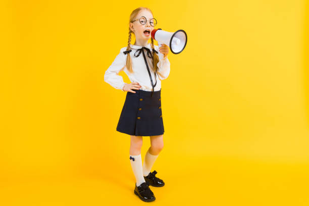 Girl with red pigtails on a yellow background. A charming girl in round transparent glasses screams into the loudspeaker. Portrait of a beautiful girl in a white blouse and black skirt. see through leggings stock pictures, royalty-free photos & images