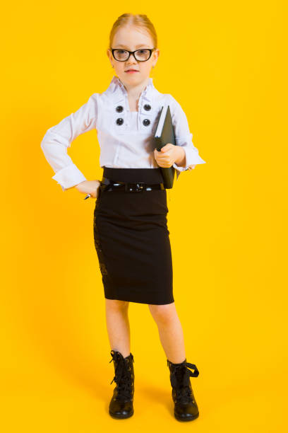 Girl with red hair on a yellow background. A charming girl in transparent glasses holds a pen and a notebook in her hands. Portrait of a beautiful girl in a white blouse and black skirt. see through leggings stock pictures, royalty-free photos & images