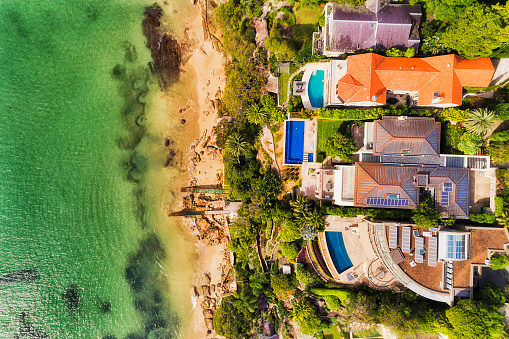 Wealthy residential houses on Sydney Middle Harbour waterfront touching cleand remote sandy beach in aerial overhead view on a sunny bright day.