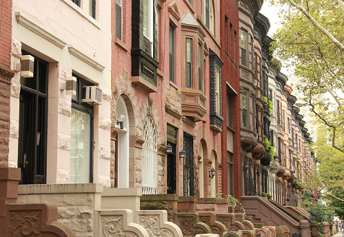 A row of colorful brownstones and stoops on a quiet block in NYC