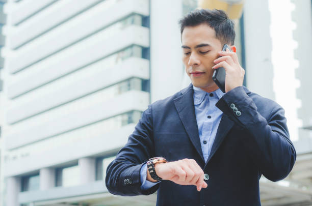 istock portrait attractive handsome business man using smartphone talking and looking smart watch at outdoor city with building background. technology connecting social online . 958284268