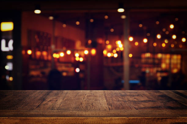 istock Image of wooden table in front of abstract blurred restaurant lights background. 958323748