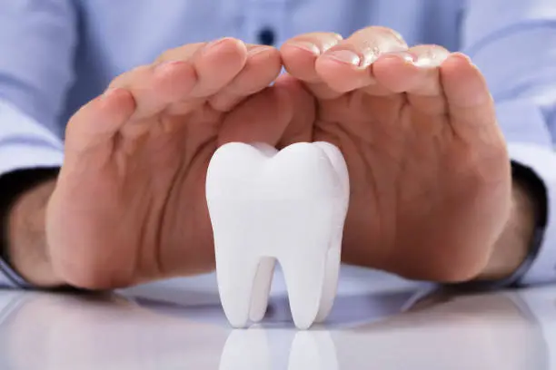 Man's Hand Protecting Healthy Hygienic White Tooth On Reflective Table