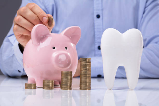 istock White Tooth Beside Man Inserting Coin In Piggy Bank 958335712