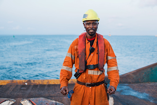 Seaman AB or Bosun on deck of offshore vessel or ship , wearing PPE personal protective equipment - helmet, coverall, lifejacket, goggles. He is happy of his job