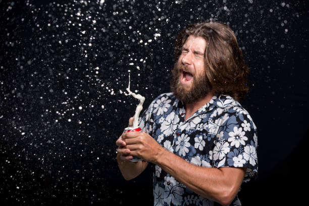 istock Man opens a bottle of cold beer spraying with splashes on black background 958345490