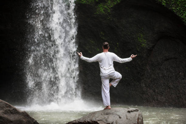 istock Man standing in meditation yoga on rock at waterfall 958356704
