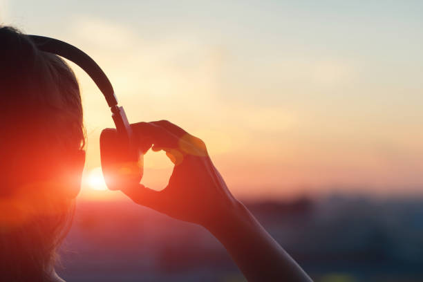 chica en auriculares escuchando música en la ciudad al atardecer - musical fotografías e imágenes de stock