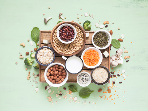 Vegetable albumen sources. Plant protein (beans, nuts, vegetables, mushrooms, seeds) on green background. Vegan and vegetarian food concept. Flat lay.