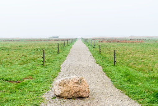 Jaravallen nature reserve in Skane, Sweden - Granite boulder used as a traffic barrier on gravel road into misty coastal landscape with bird tower visible in the distance.