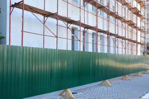 Reconstruction building with external insulation and plaster and with using of scaffolding. Temporary metal fence around the construction site