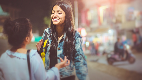 Asian, Indian multi ethnic female friend together on city street. They are having fun and enjoying their leisure time while walking and talking on street at night.