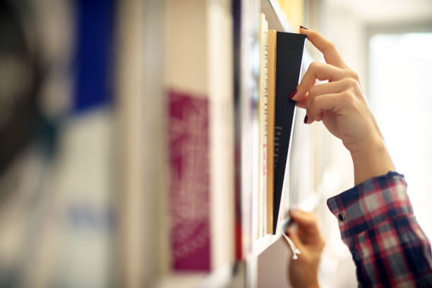 istock Close up view of a female hand taking a book from bookshelf within the library. 958454504