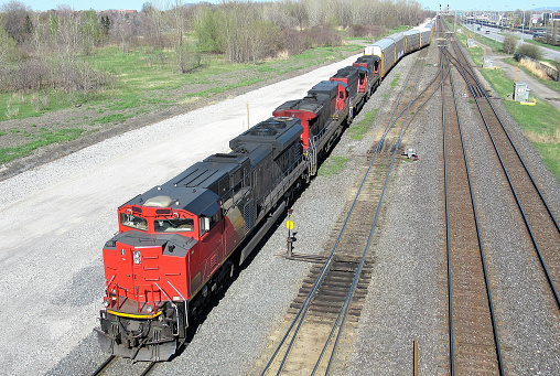 Transportation...This shot, looking down from an overhead bike path, shows a very long,{4 engine freight train}, waiting to switch tracks in a rail yard.